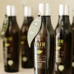 Photo de l’ensemble de la gamme de shampoings bio Hairborist, alignés élégamment sur une étagère en bois naturel, avec des plantes aromatiques et huiles essentielles autour. On distingue clairement les flacons aux étiquettes colorées correspondant à chaque besoin capillaire : Sensity pour les cuirs chevelus sensibles, Daily Clean pour un usage fréquent, Harmony Clean pour réguler le sébum, Color Clean pour cheveux colorés, Men Tonic pour les hommes actifs, et Naturalys pour équilibrer le microbiote. L’image évoque l’univers naturel, écoresponsable et artisanal de la marque Hairborist, en harmonie avec les valeurs de La Maison du Coloriste.