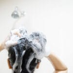 Jeune femme lavant ses cheveux avec un shampoing sans sulfate, rituel capillaire doux et respectueux.