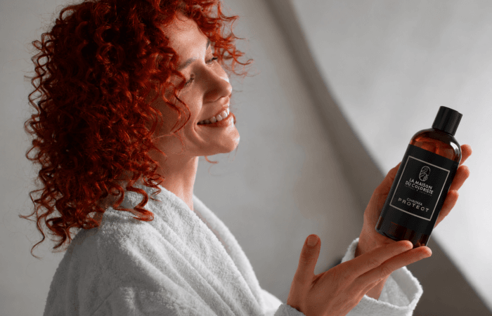 Femme aux cheveux bouclés roux tenant le shampoing Chroma Protect La Maison du Coloriste, soin cheveux colorés